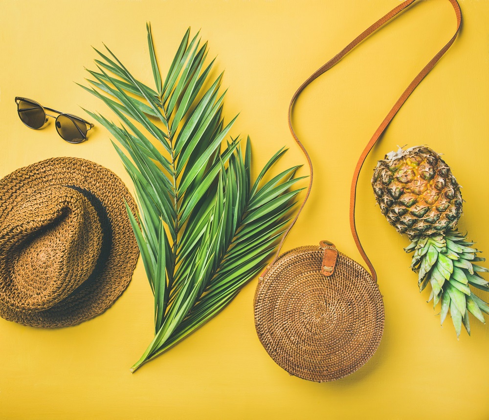 Tenue d'été colorée pour femme, vue de dessus. Chapeau de paille, sac en bambou, lunettes de soleil, branches de palmier et ananas sur fond jaune, vue de dessus. Concept de mode ou de voyage pour les vacances d'été